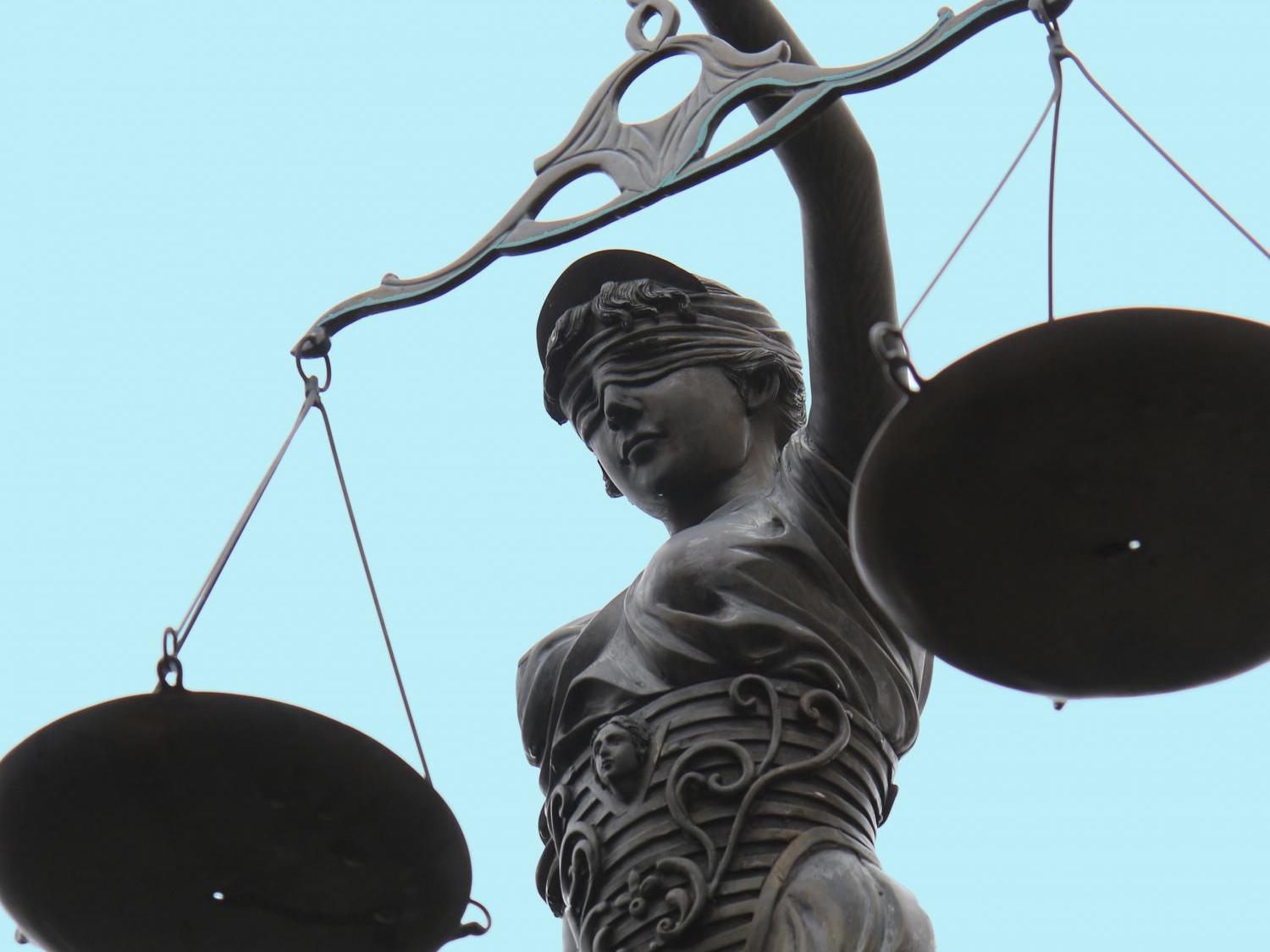 Statue der Justitia mit Waage vor blauem Hintergrund