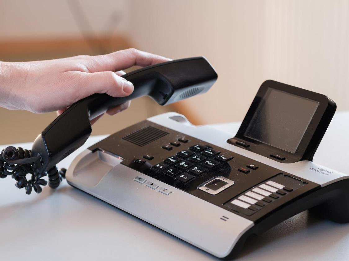 Eine Hand greift einen Telefonhörer und hebt ihn gerade ab