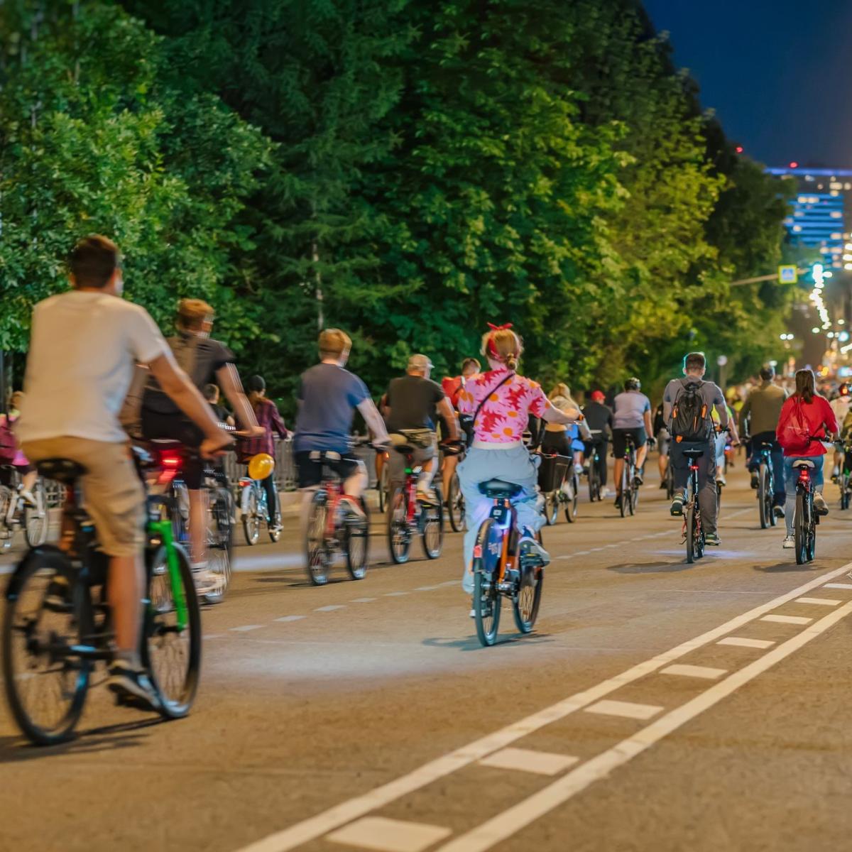 Viele Radfahrer radeln über die ganze Straßer verteilt durch die abendliche Stadt mit Ansicht von hinten