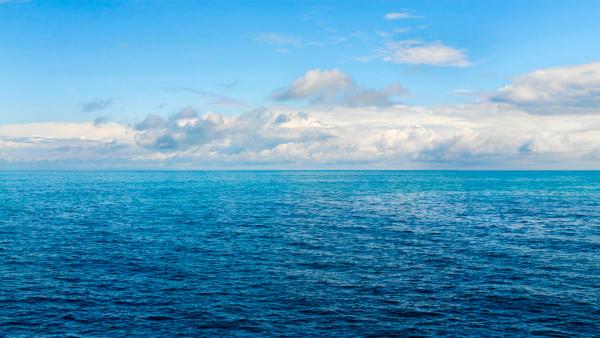 Blick auf das weite blaue Meer, darüber der endlose Horizont mit Wolken