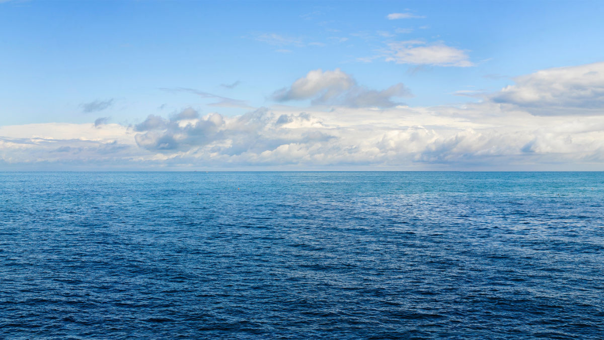 Blick auf das weite blaue Meer, darüber der endlose Horizont mit Wolken