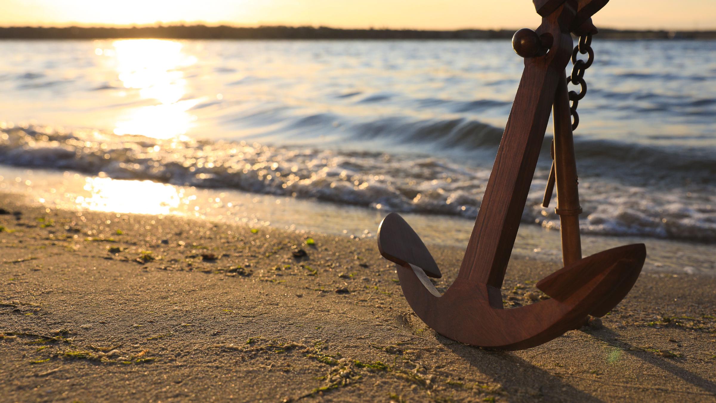 großer Eisenanker an einem Sandstrand in der warmweißen Abendsonne