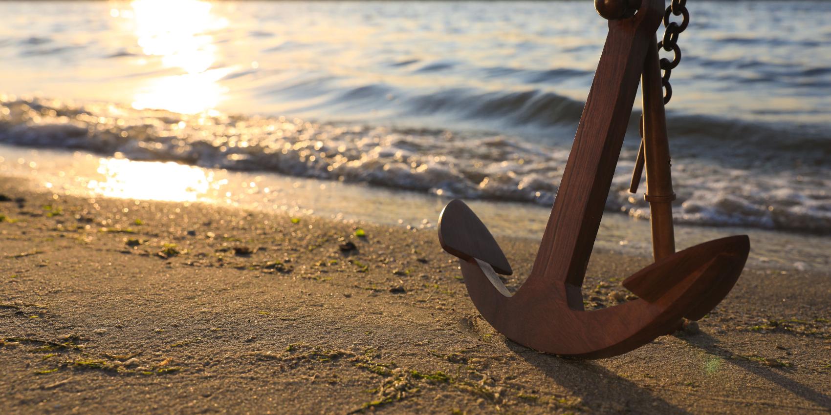 großer Eisenanker an einem Sandstrand in der warmweißen Abendsonne