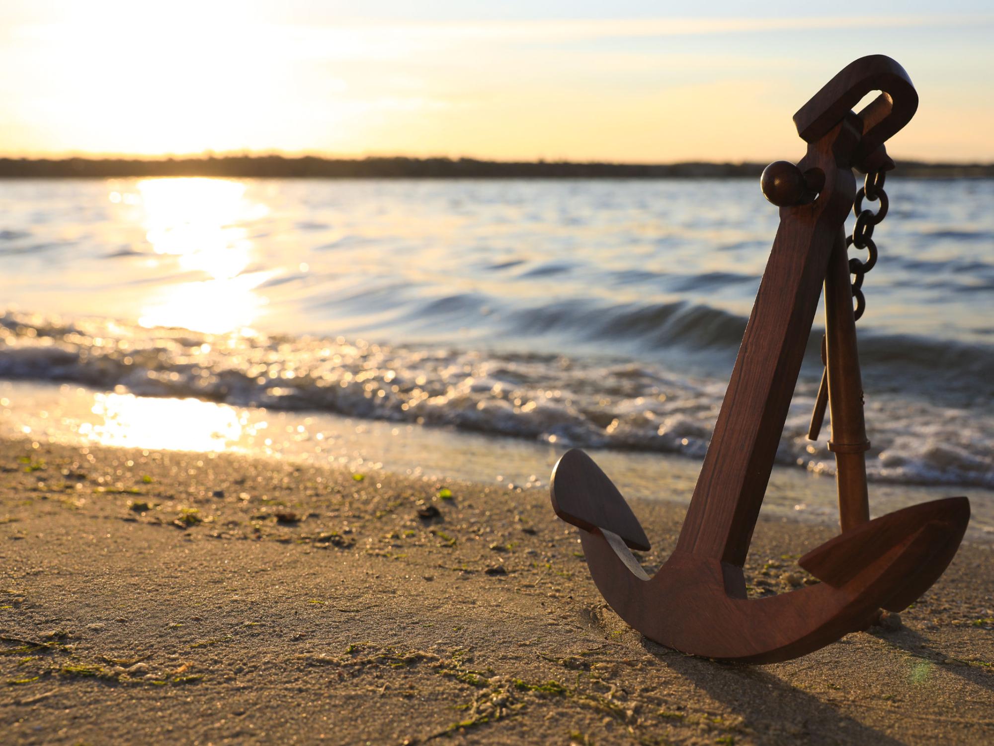 großer Eisenanker an einem Sandstrand in der warmweißen Abendsonne