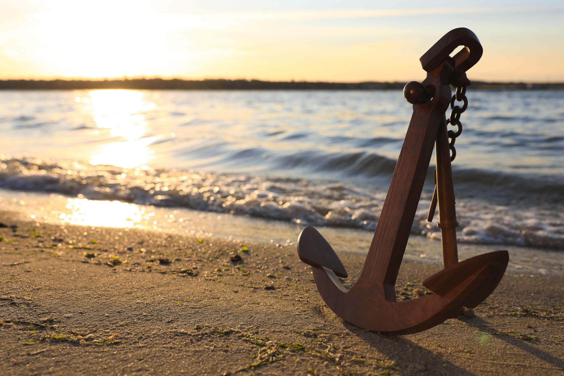 großer Eisenanker an einem Sandstrand in der warmweißen Abendsonne