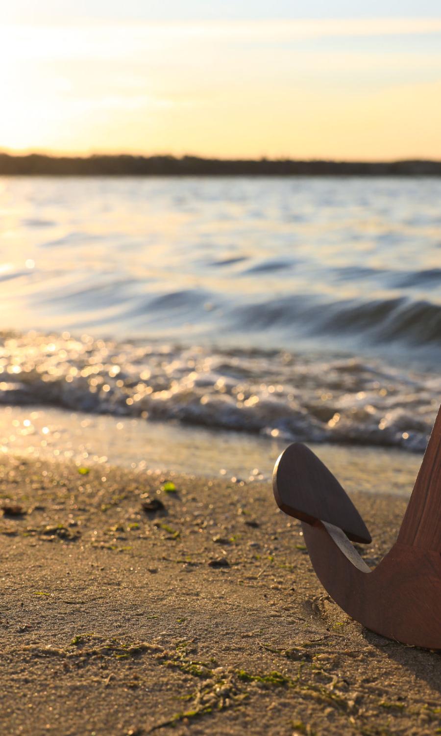 großer Eisenanker an einem Sandstrand in der warmweißen Abendsonne