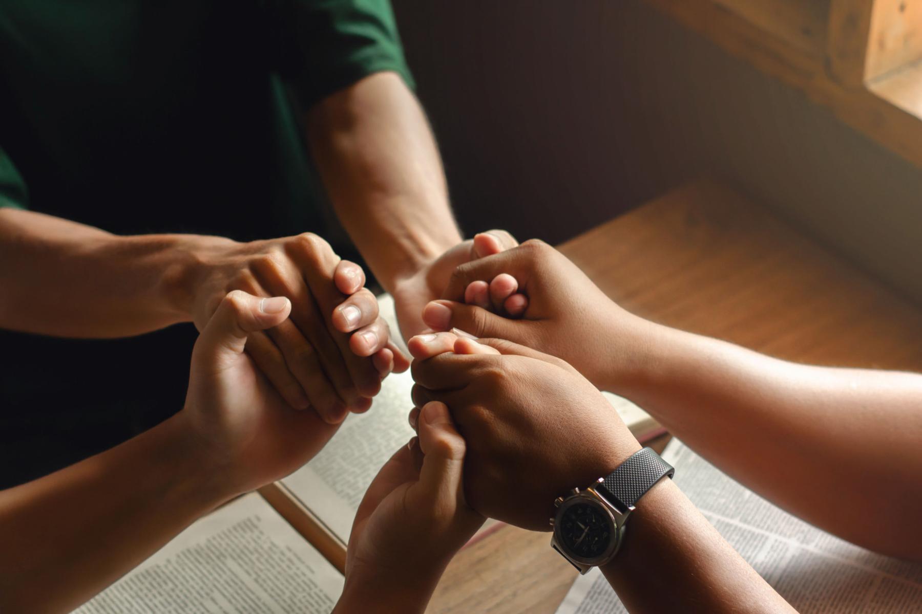 Hände drei junger Menschen die sich im Kreis an den Händen halten