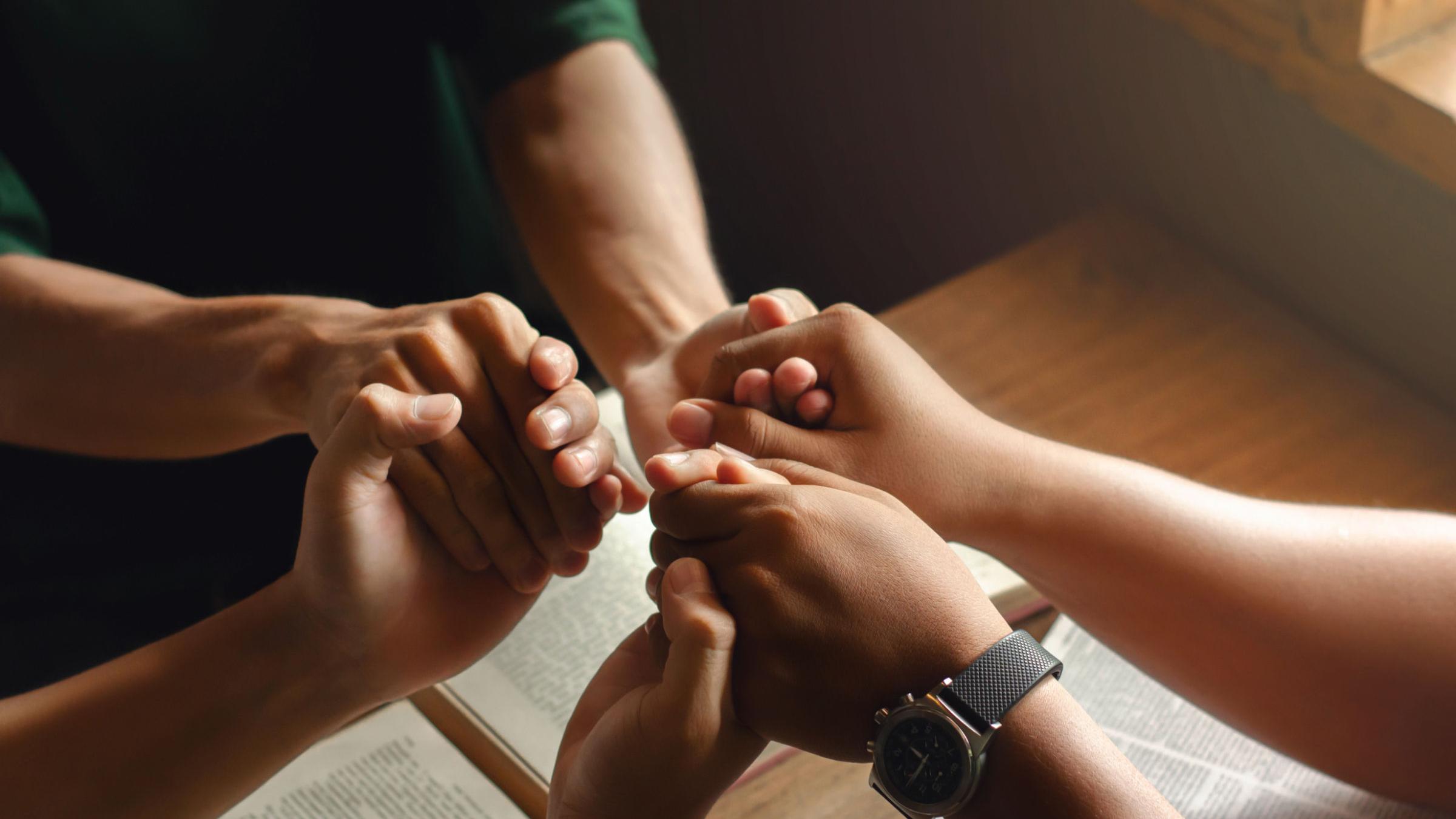 Hände drei junger Menschen die sich im Kreis an den Händen halten