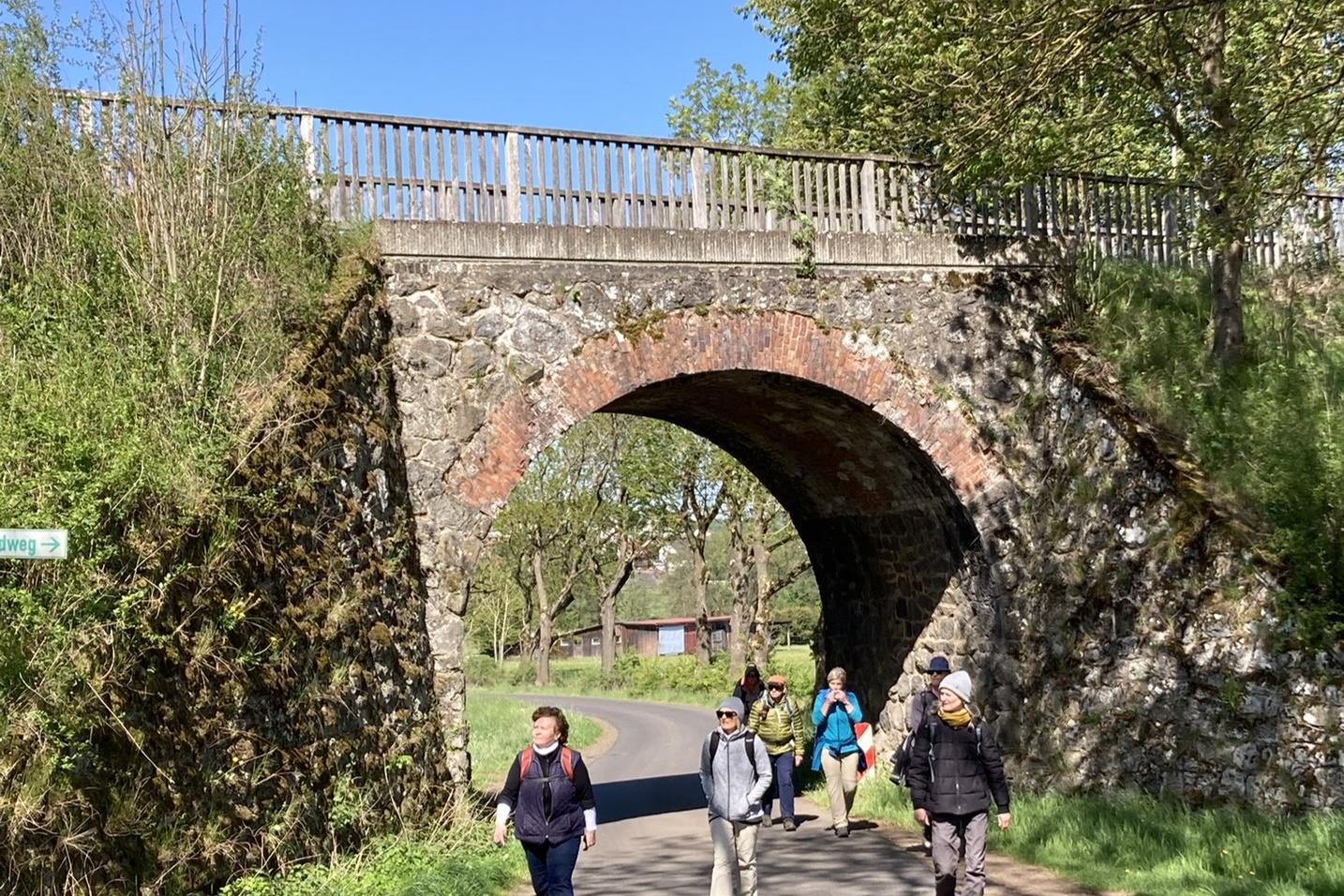 Wanderweg auf dem Asphalt, Viadukt, verschiedene Wanderinnen bei Durchgang unter dem Viadukt