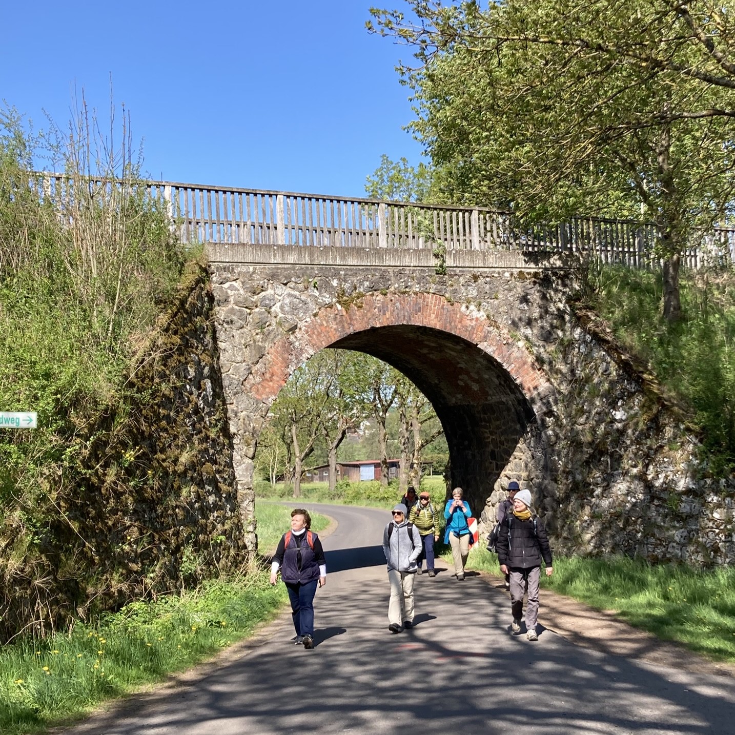 Wanderweg auf dem Asphalt, Viadukt, verschiedene Wanderinnen bei Durchgang unter dem Viadukt