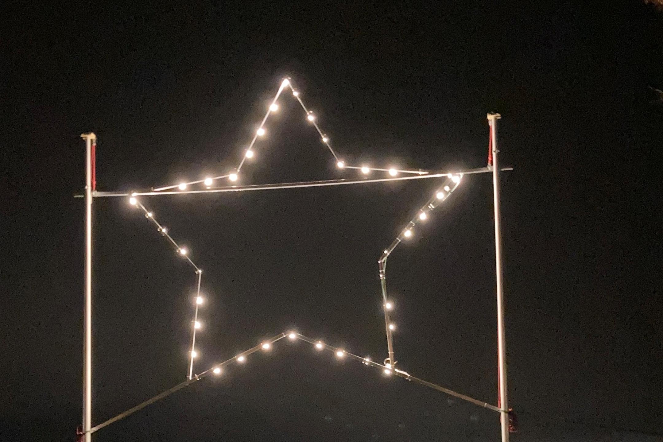 Stern aus Glühbirnen bei Nacht, im Hintergrund die Lichter von Gau-Algesheim und dem Rheingau, im Vordergrund zwei leere Bänke