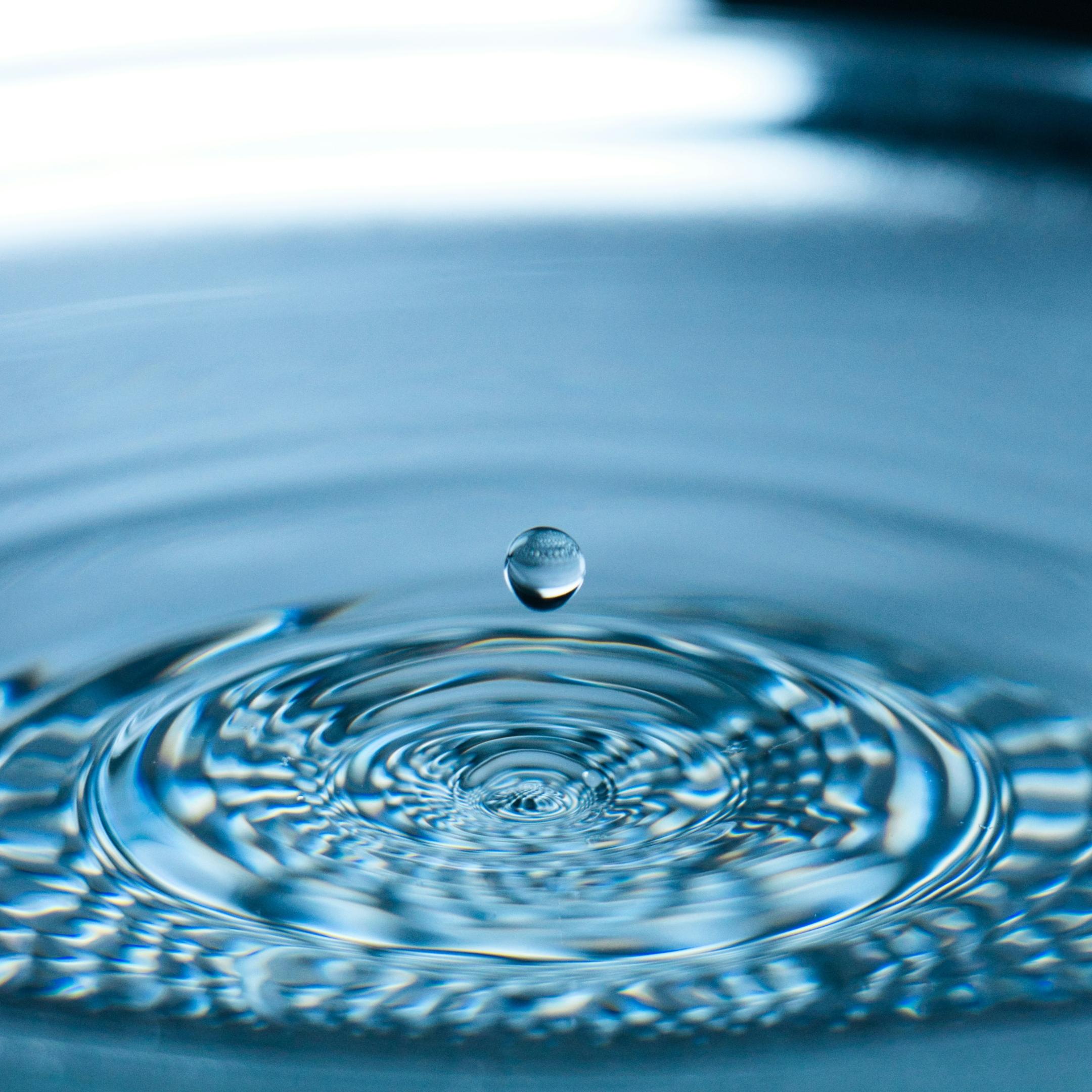 Ein Wassertropen tropft in eine Wasserfläche