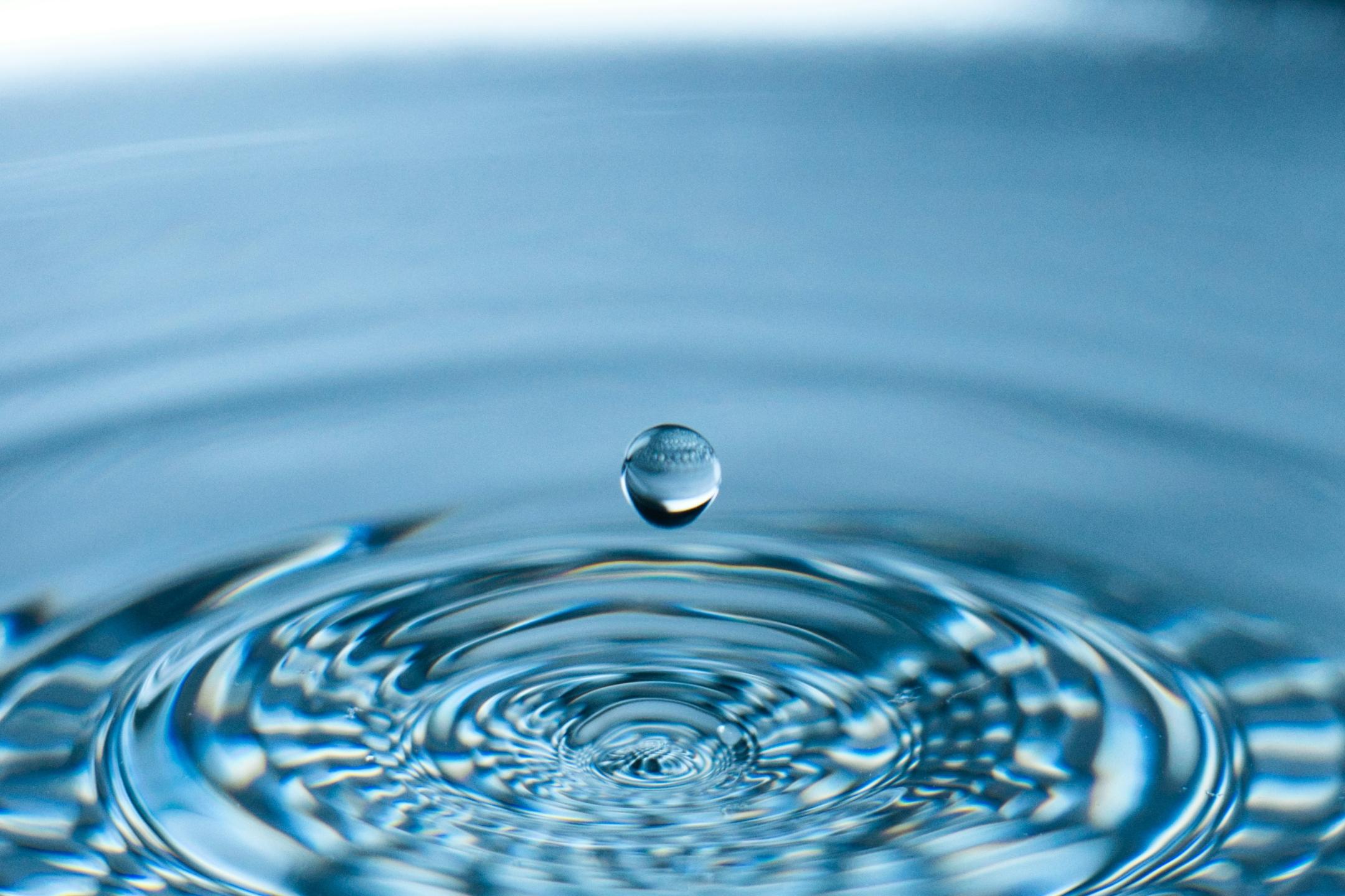 Ein Wassertropen tropft in eine Wasserfläche