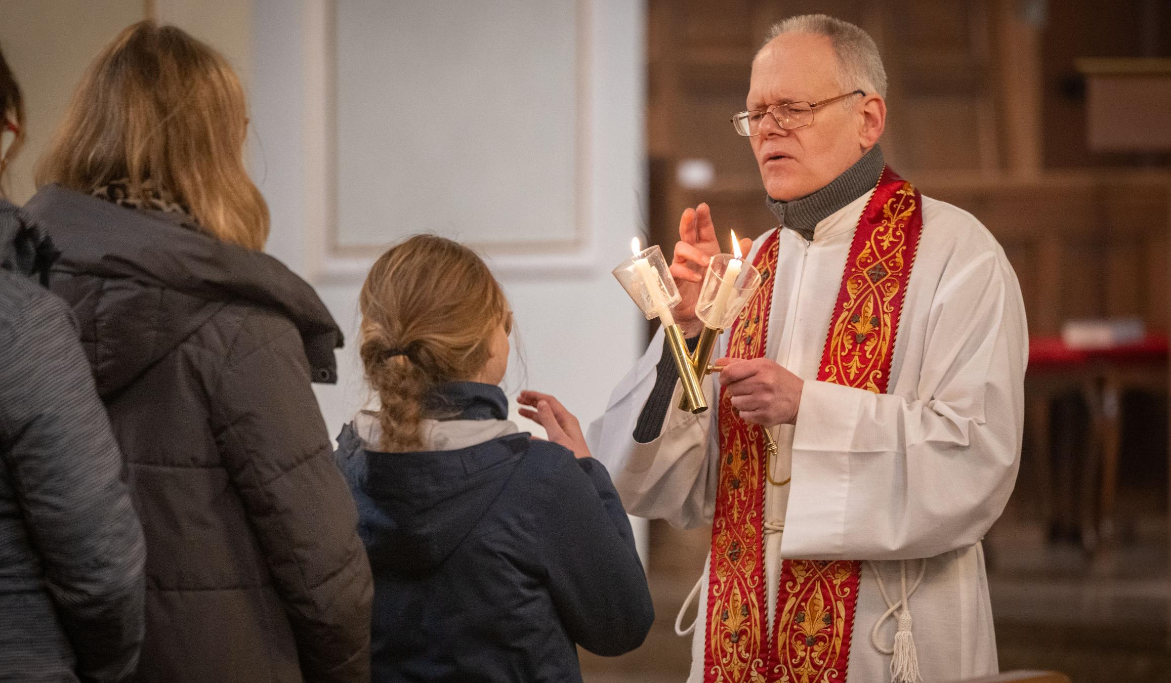 Gottesdienstbesucherinnen stehen an, um den Blasiussegen zu empfangen, den der Priester mit einem Gebet und zwei überkreuzten Kerzen spendet