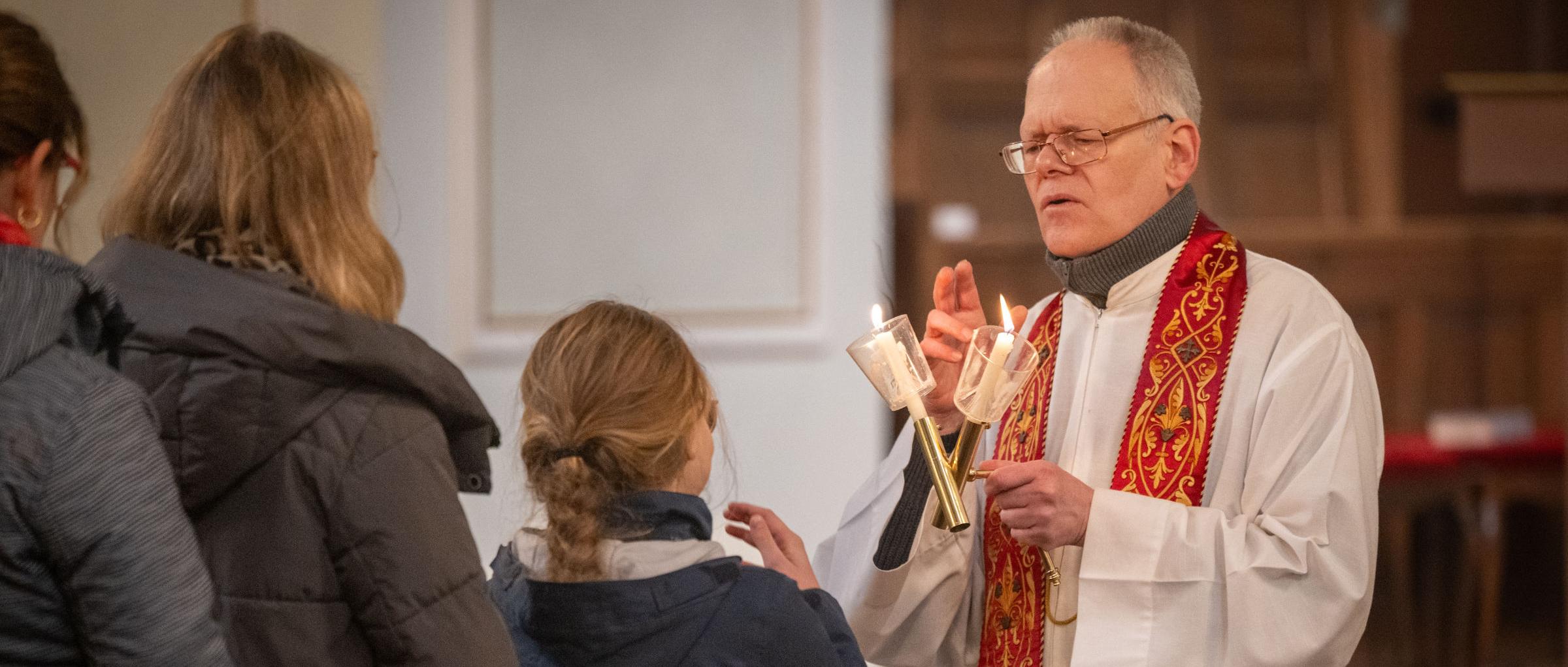 Gottesdienstbesucherinnen stehen an, um den Blasiussegen zu empfangen, den der Priester mit einem Gebet und zwei überkreuzten Kerzen spendet
