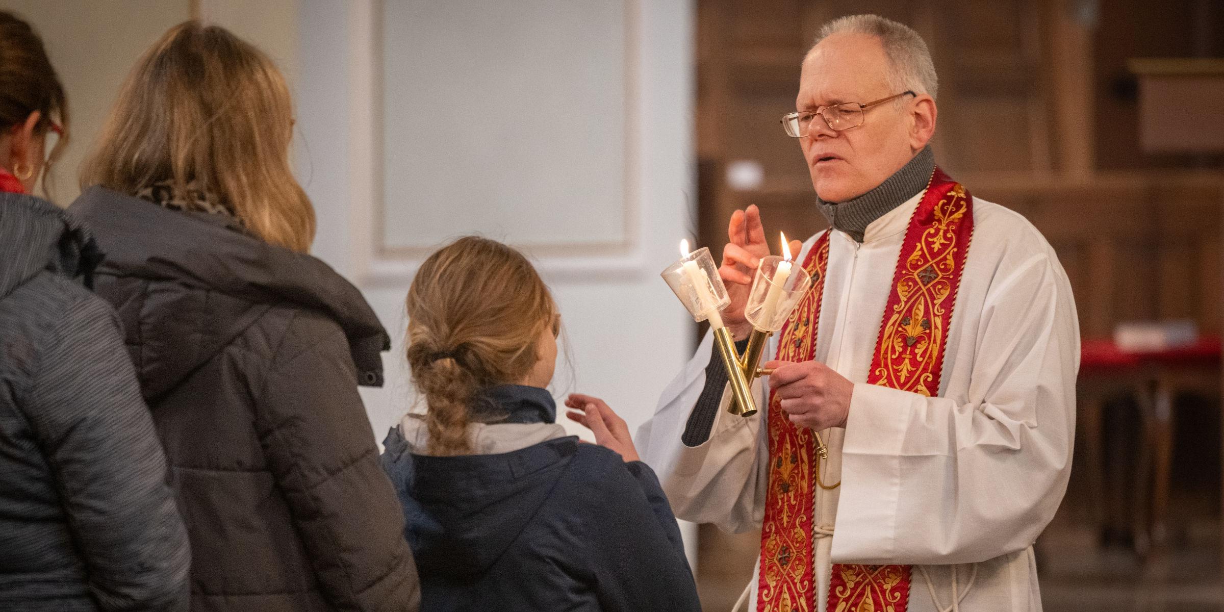 Gottesdienstbesucherinnen stehen an, um den Blasiussegen zu empfangen, den der Priester mit einem Gebet und zwei überkreuzten Kerzen spendet