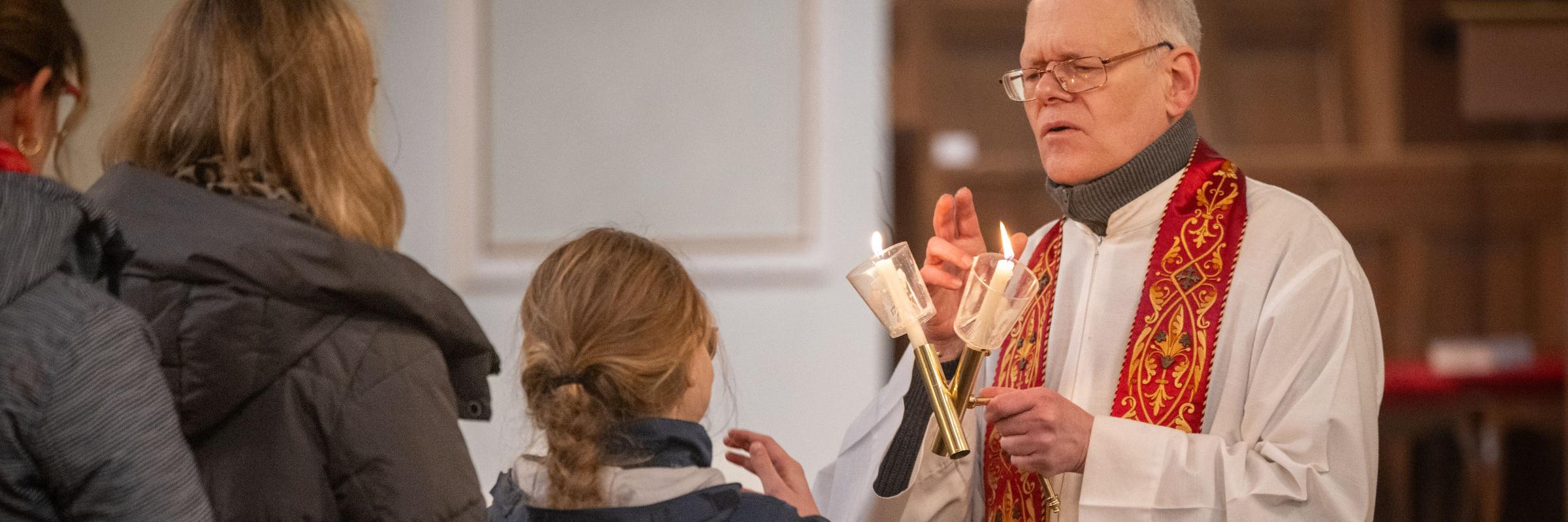 Gottesdienstbesucherinnen stehen an, um den Blasiussegen zu empfangen, den der Priester mit einem Gebet und zwei überkreuzten Kerzen spendet