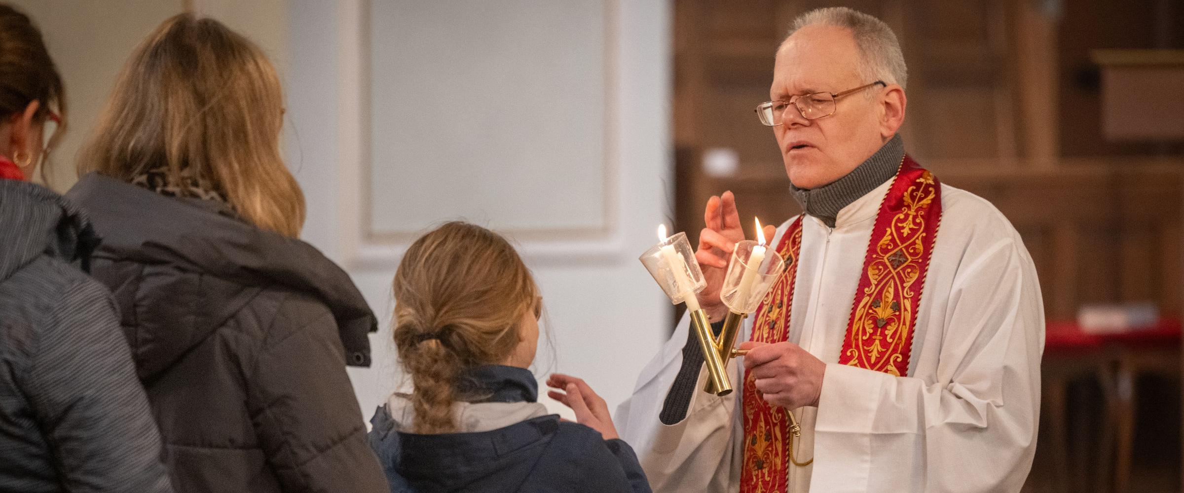 Gottesdienstbesucherinnen stehen an, um den Blasiussegen zu empfangen, den der Priester mit einem Gebet und zwei überkreuzten Kerzen spendet