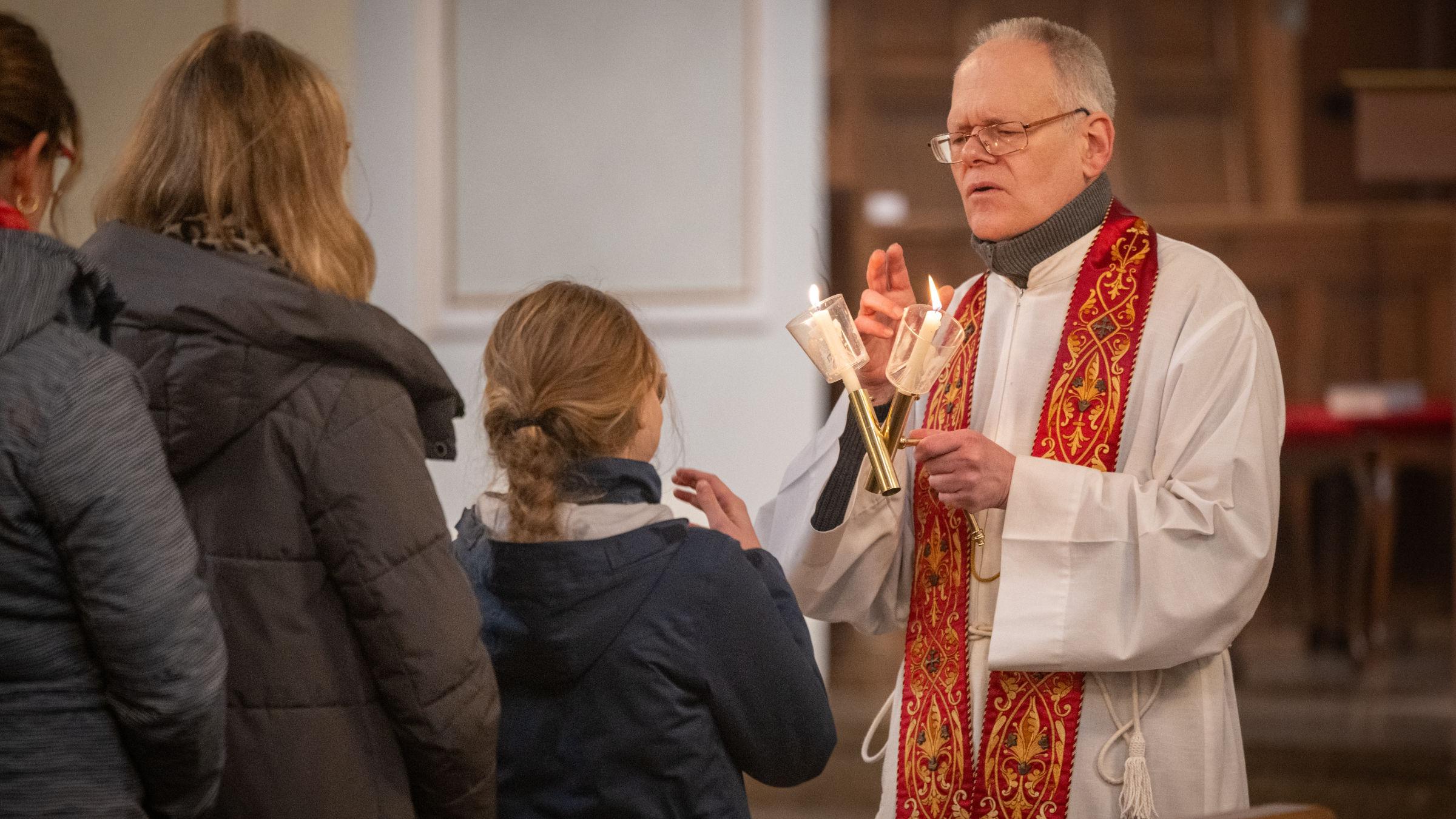 Gottesdienstbesucherinnen stehen an, um den Blasiussegen zu empfangen, den der Priester mit einem Gebet und zwei überkreuzten Kerzen spendet