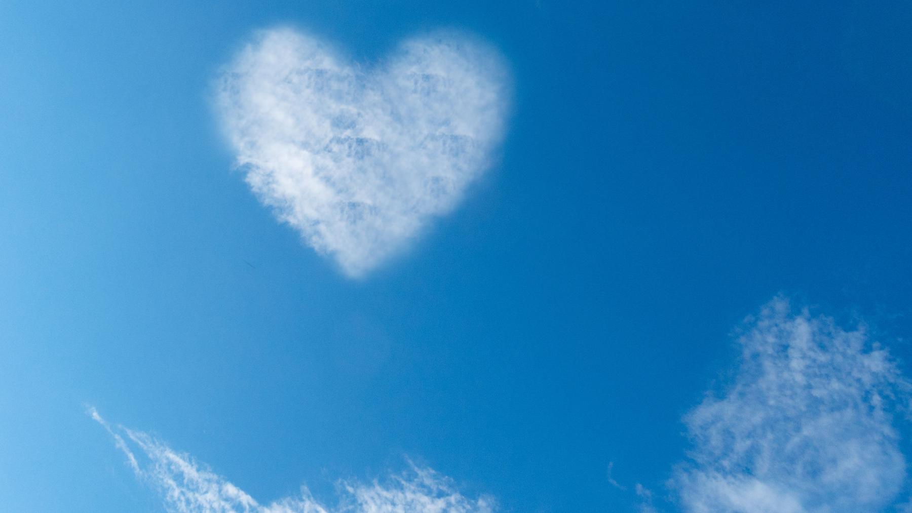 Blauer Himmel mit leichte Wölkchen, wo sich eine zu einer Herzform konzentriert