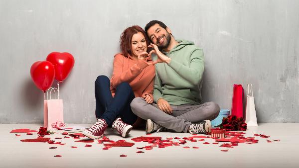 Paar am Valentinstag nebeneinander auf dem Boden sitzend machen ein Herz mit ihren Händen