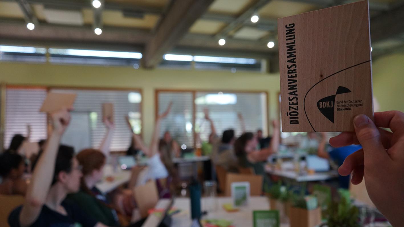 Im Vordergrund sieht man eine erhobene Stimmkarte auf der Diözesanversammlung des BDKJ Mainz