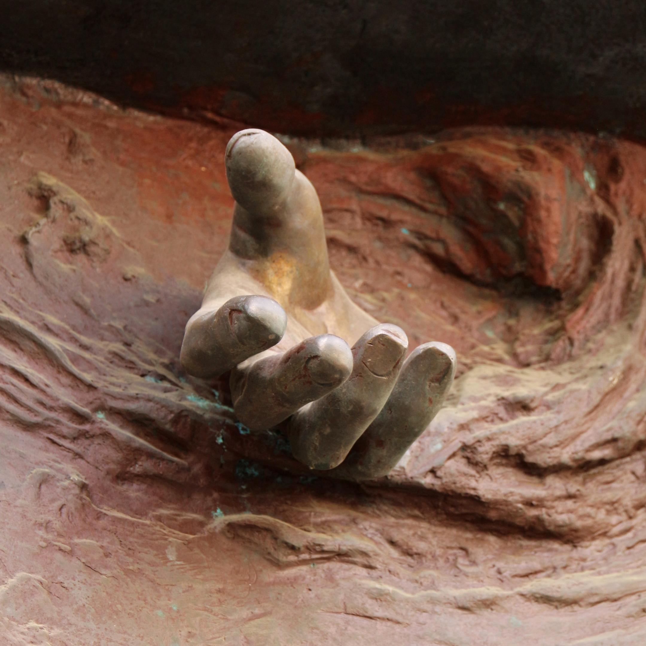 Eine Hand kommt  scheinbar aus einem Edelrost-Kunstwerk heraus.