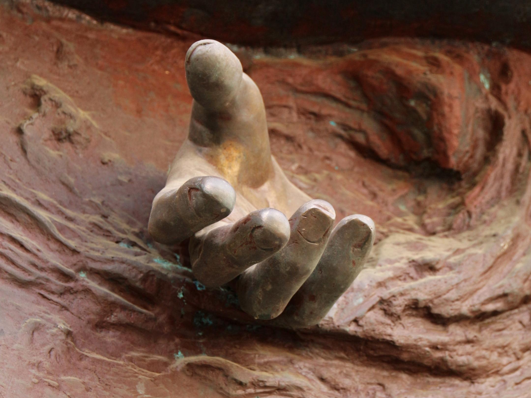 Eine Hand kommt  scheinbar aus einem Edelrost-Kunstwerk heraus.