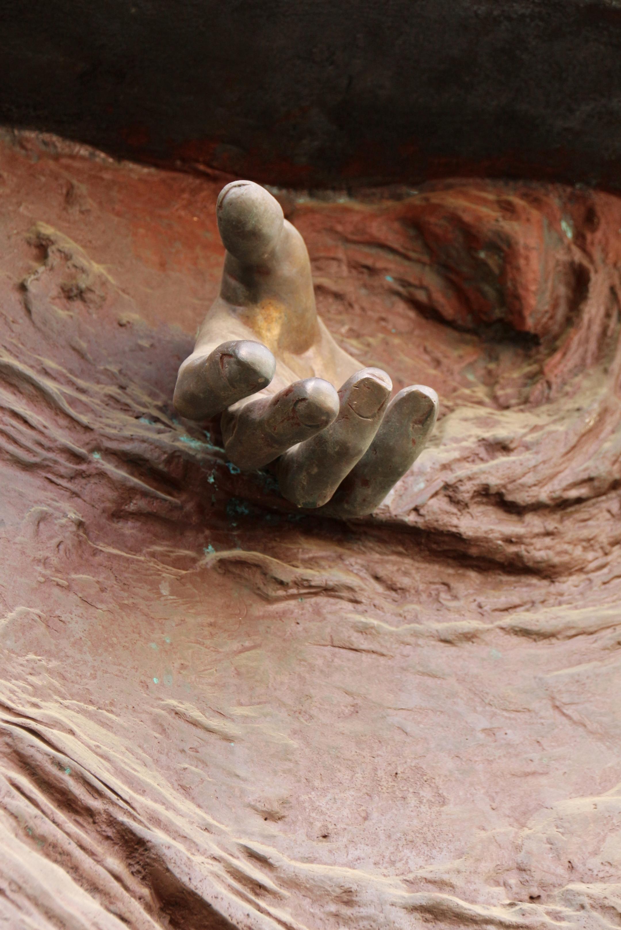 Eine Hand kommt  scheinbar aus einem Edelrost-Kunstwerk heraus.