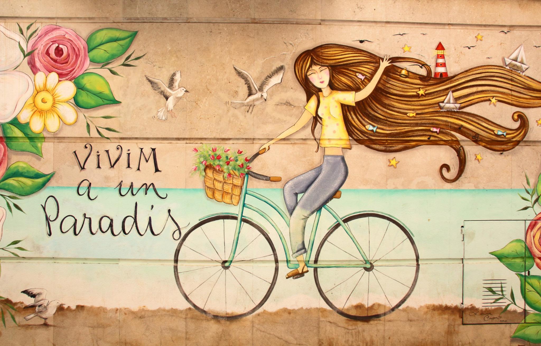 Eine junge Frau fährt auf einem Fahrrad vor einer idyllischen Landschaft mit bunten Blumen.