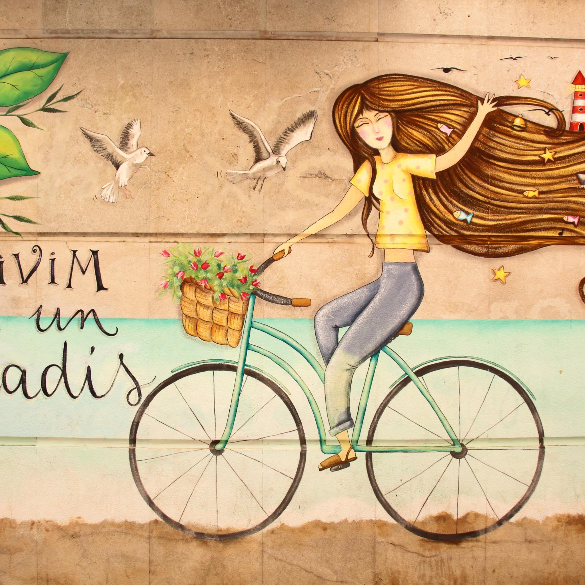 Eine junge Frau fährt auf einem Fahrrad vor einer idyllischen Landschaft mit bunten Blumen.