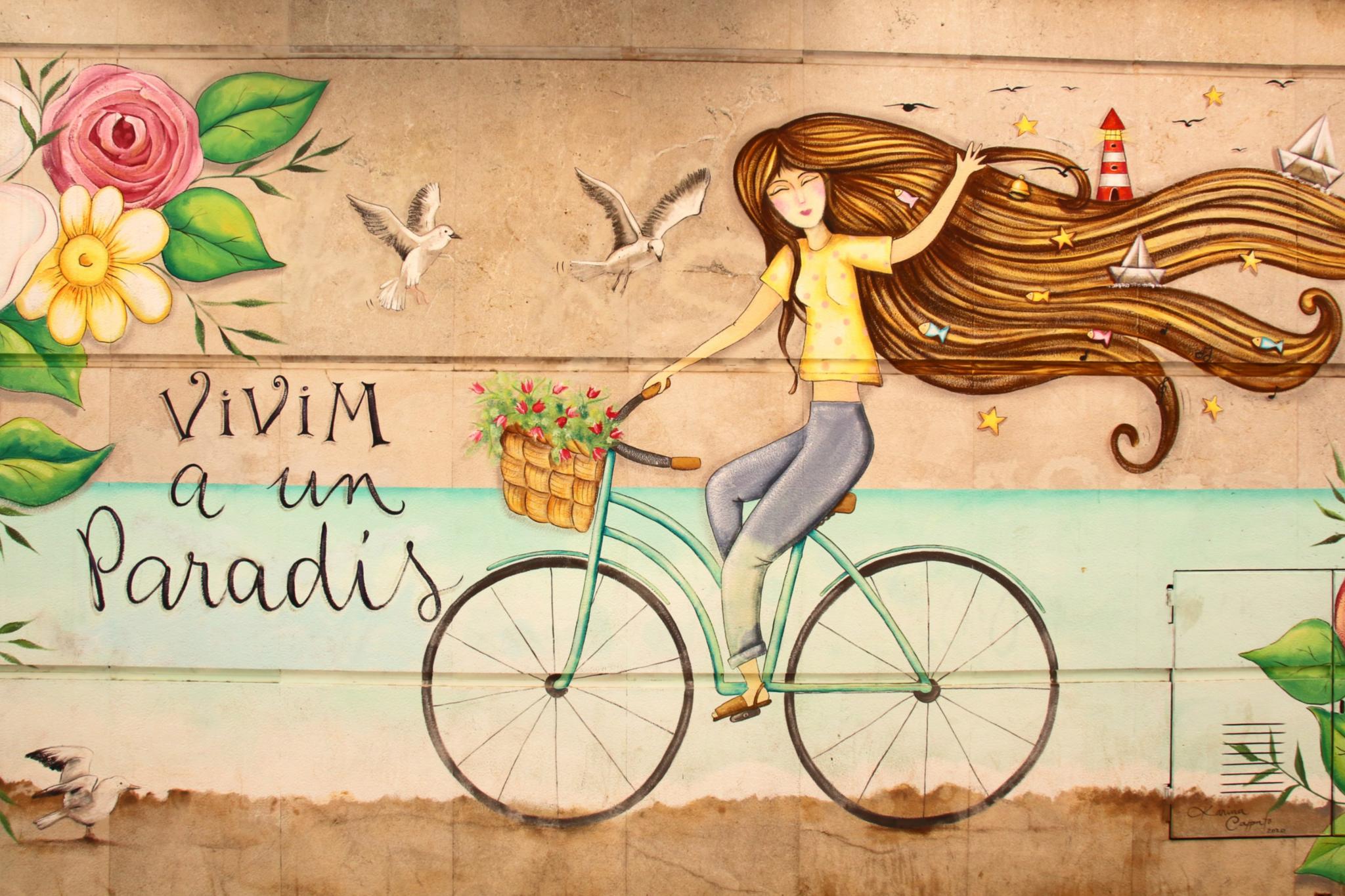 Eine junge Frau fährt auf einem Fahrrad vor einer idyllischen Landschaft mit bunten Blumen.