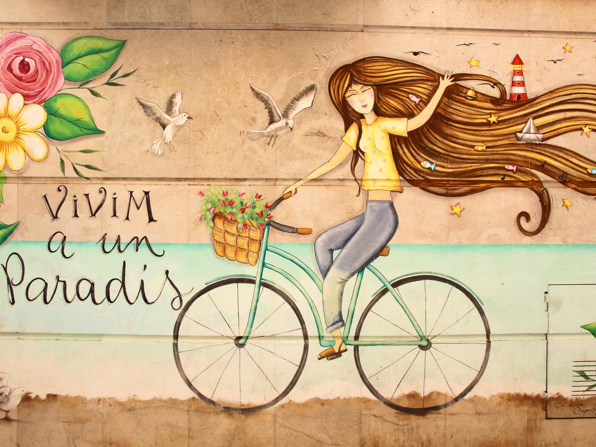 Eine junge Frau fährt auf einem Fahrrad vor einer idyllischen Landschaft mit bunten Blumen.