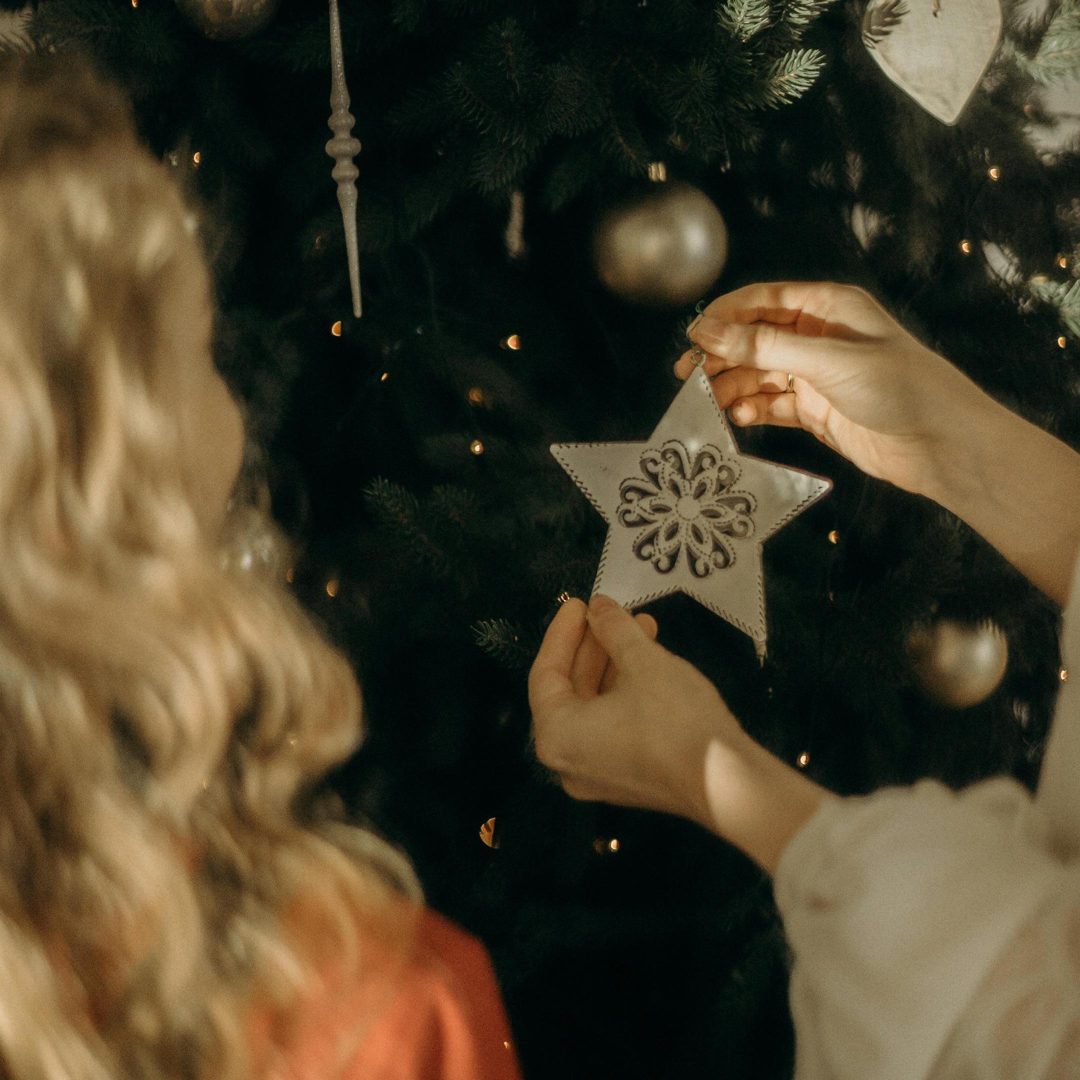 Zwei Kinder stehen vor einem großen Christbaum und hängen einen weißen Stern auf.
