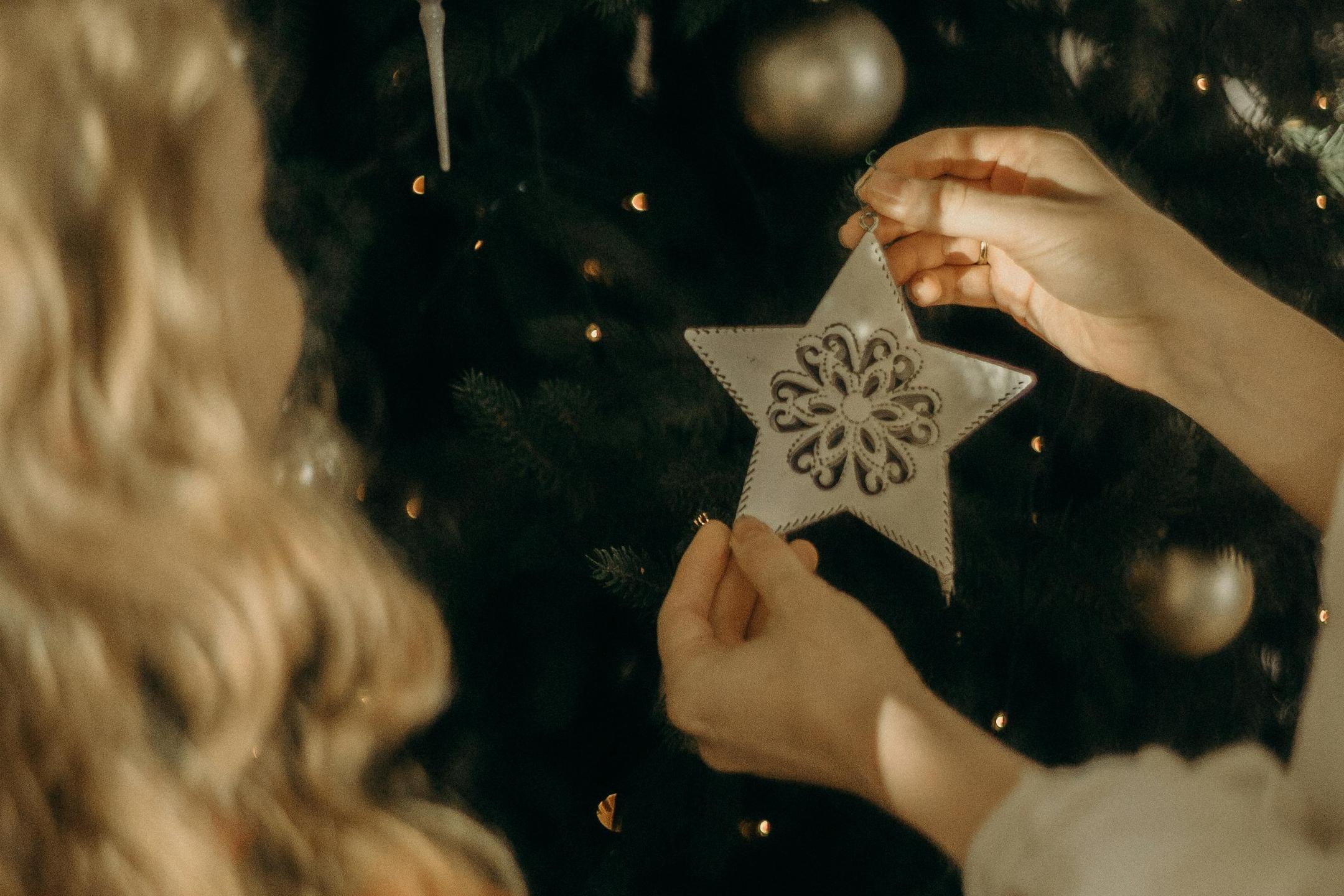 Zwei Kinder stehen vor einem großen Christbaum und hängen einen weißen Stern auf.