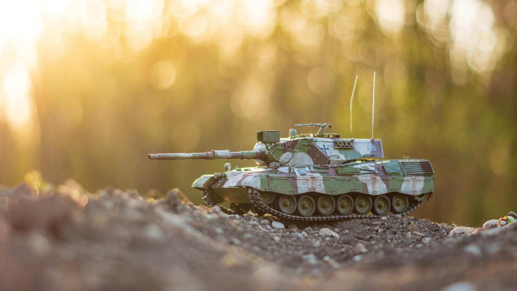 Spielzeugpanzer auf einem Erdhügel mit Siluetten von Bäumen im Hintergrund