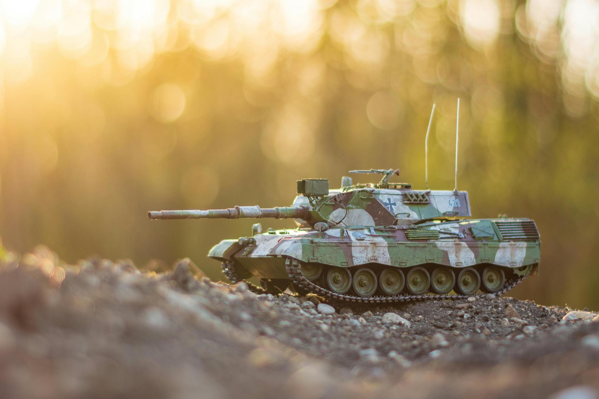 Spielzeugpanzer auf einem Erdhügel mit Siluetten von Bäumen im Hintergrund