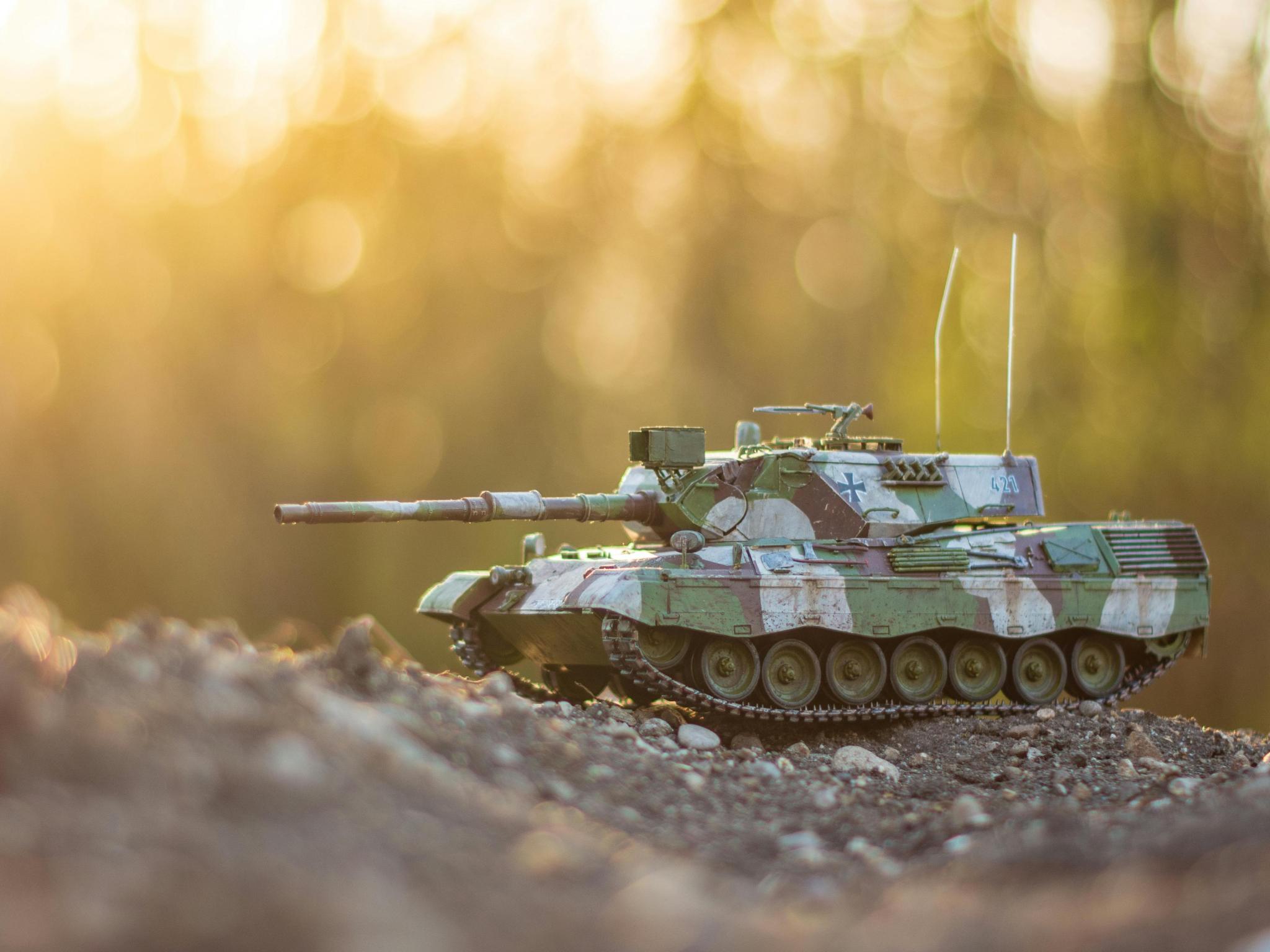 Spielzeugpanzer auf einem Erdhügel mit Siluetten von Bäumen im Hintergrund