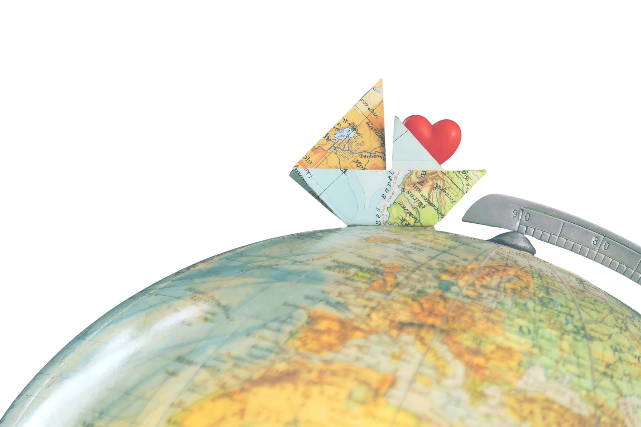Ein aus einer Landkarte gefaltetes Segelboot steht auf einem Globus. Aus dem Segel des Bootes ragt ein rotes Herz hervor.