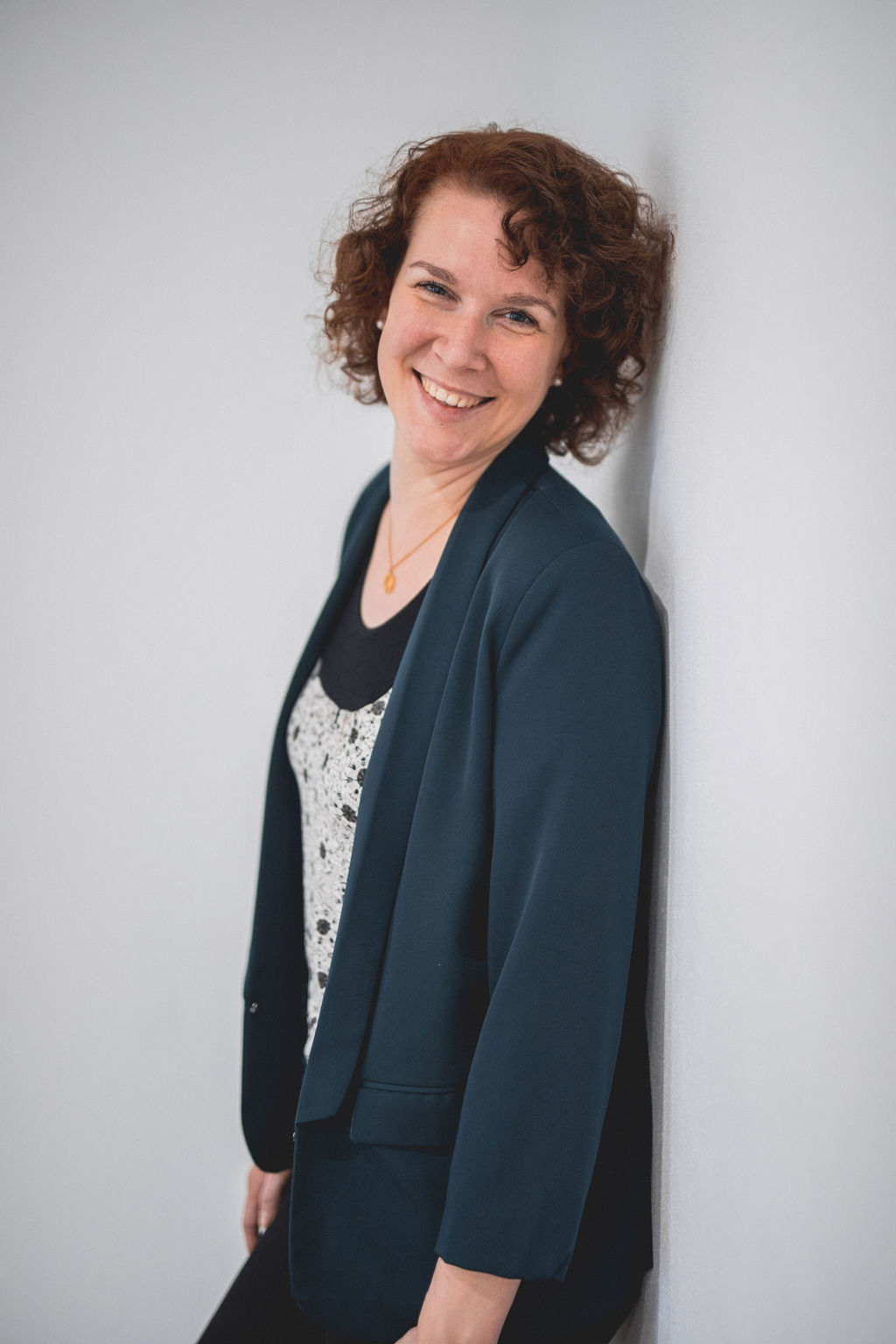 Frau mit einer West an einer Wand gelehnt,  die in die Kammera lächelt