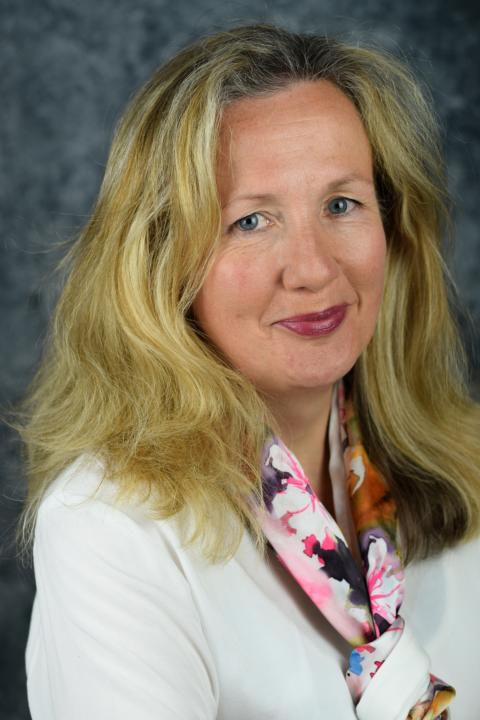 Frau mit langen Haaren und weißnem Oberteil, die in die Kammera lächelt