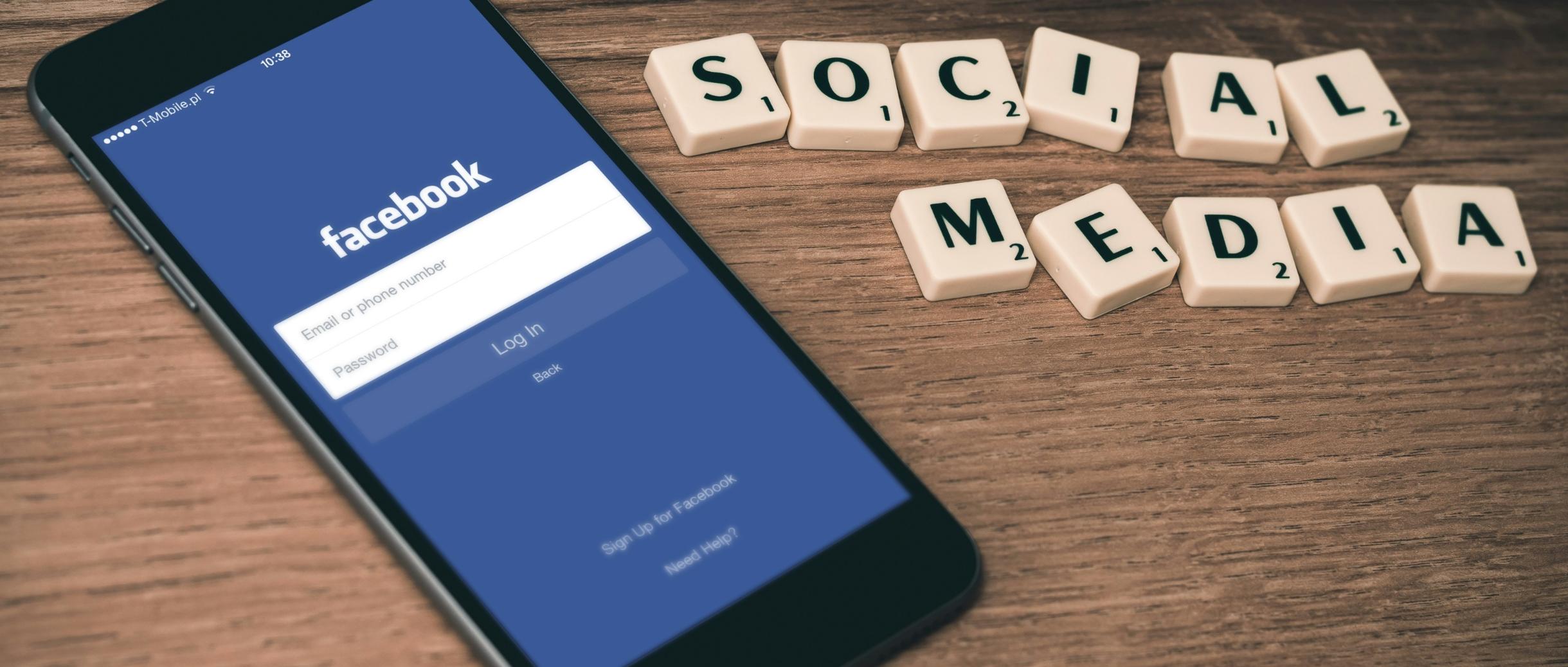 Handy mit Facbook auf einem Tisch - neben Buchstaben. Mit den Buchstaben ist das Wort Social Media gelegt.