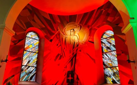 In einer Kriche. Im Altarraum ist an der Wand Jesus aufgemalt.
