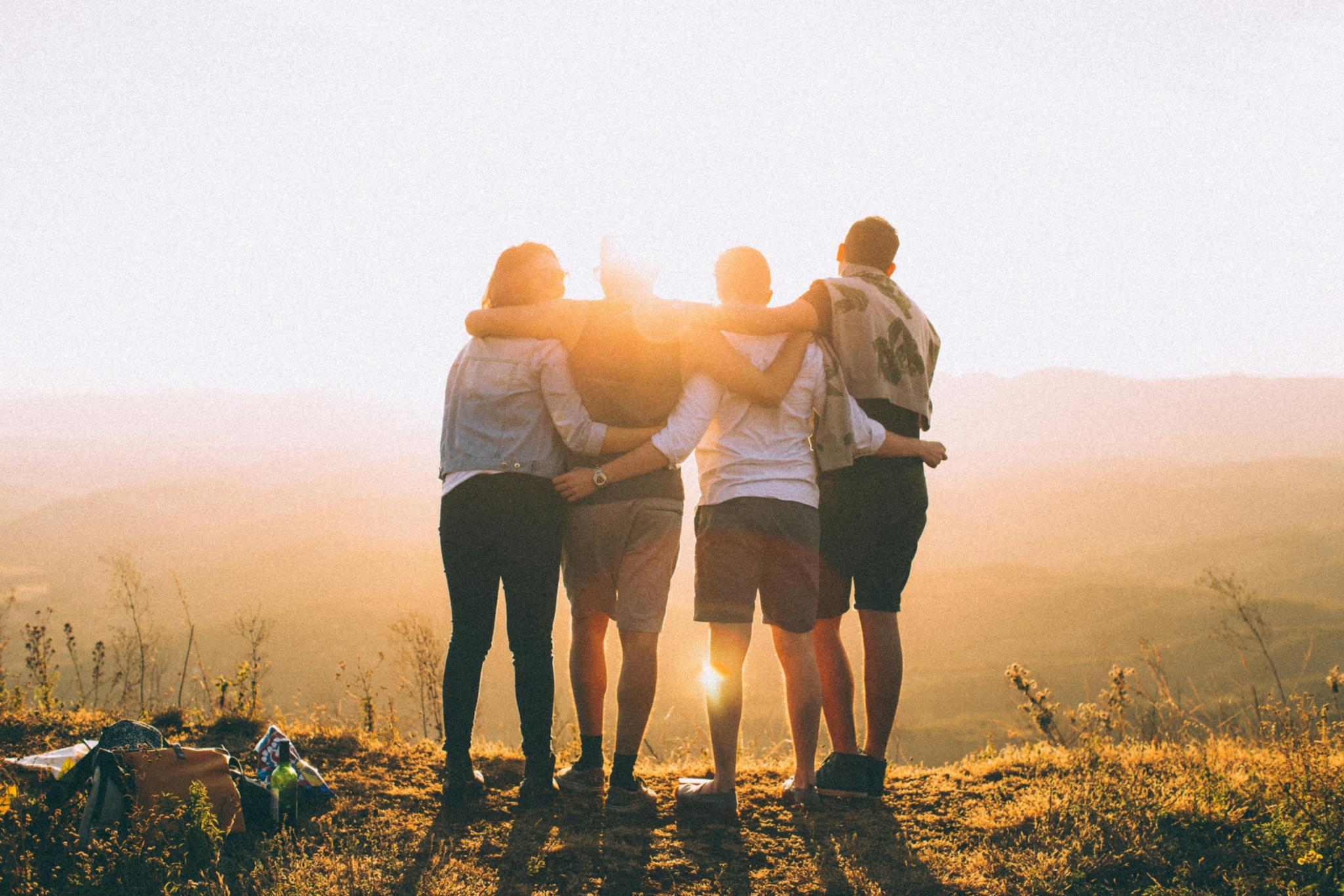 Vier Jugendliche von hinten schauen in den Sonnenuntergang