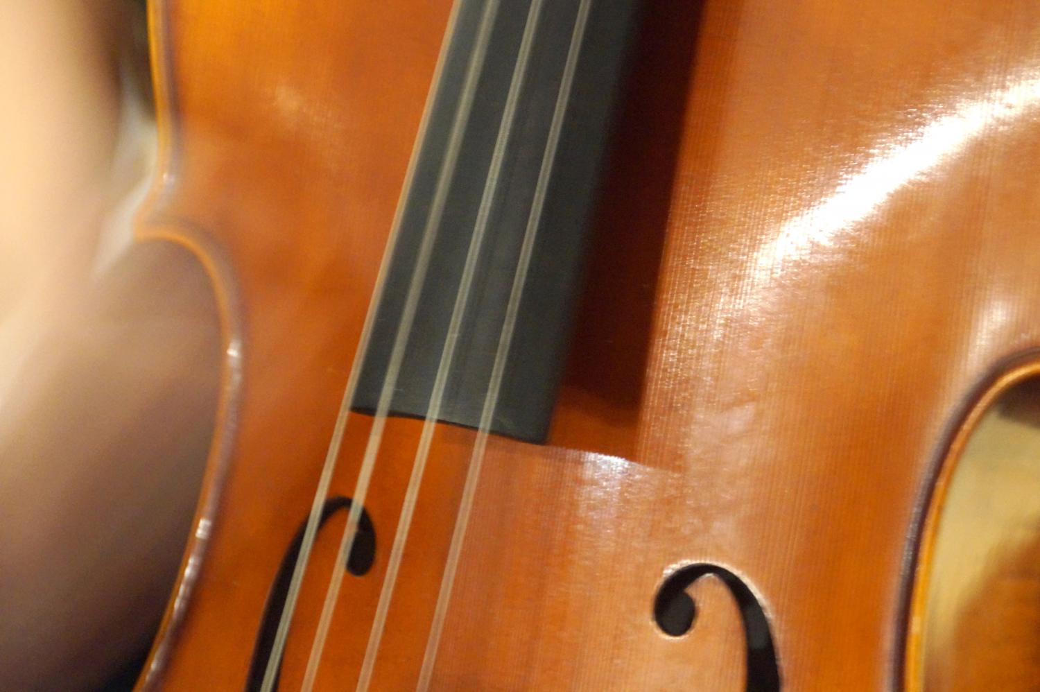 Nahaufnahme von einem Cello mit vibrierenden Saiten und glänzender Holzoberfläche
