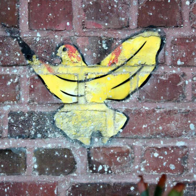 Gelbes Schmetterlings-Graffiti auf roter Backsteinmauer, daneben grüne Blätter