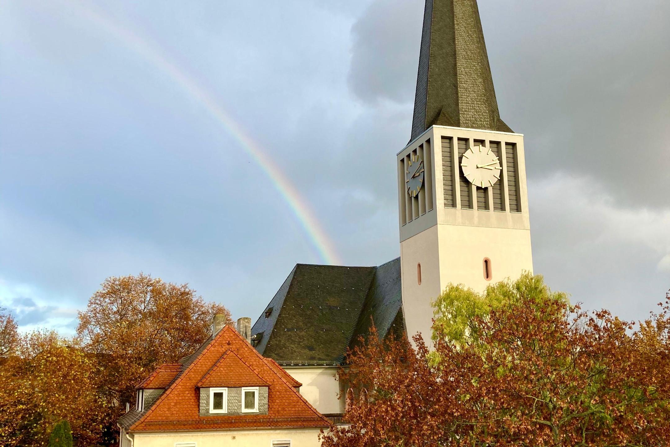 Katholische Pfarrkirche St. Georg und Pfarrhaus mit Regenbogen, der auf dem Kirchendach 'endet'