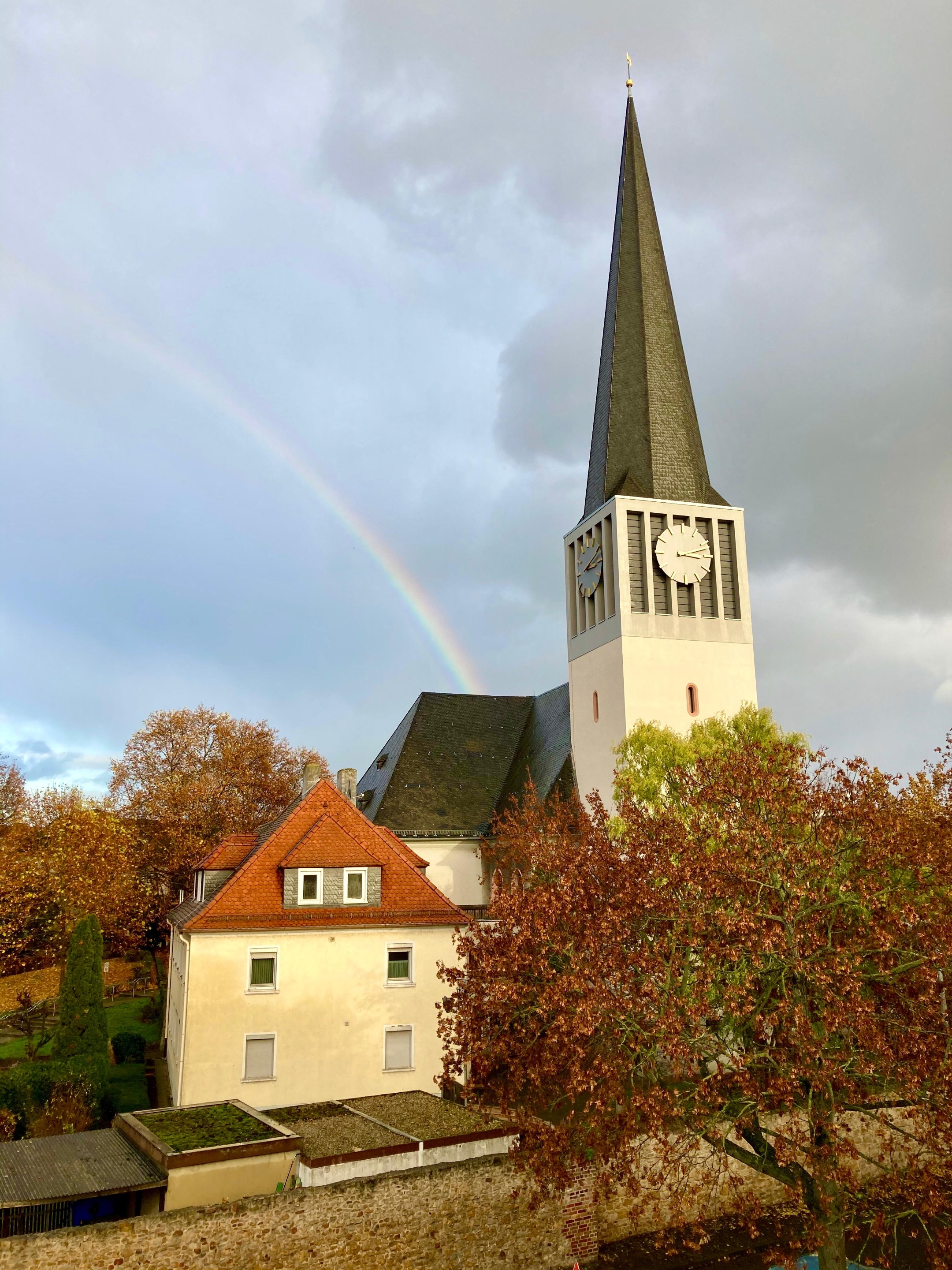 Katholische Pfarrkirche St. Georg und Pfarrhaus mit Regenbogen, der auf dem Kirchendach 'endet'