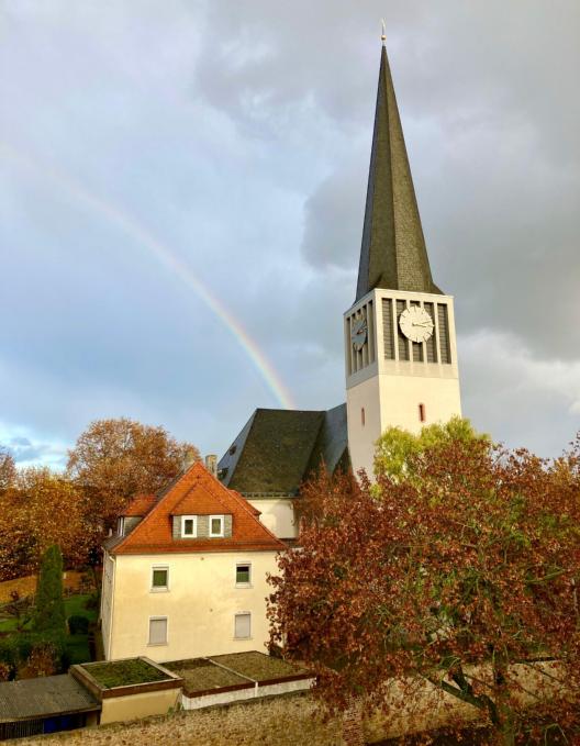 Katholische Pfarrkirche St. Georg und Pfarrhaus mit Regenbogen, der auf dem Kirchendach 'endet'