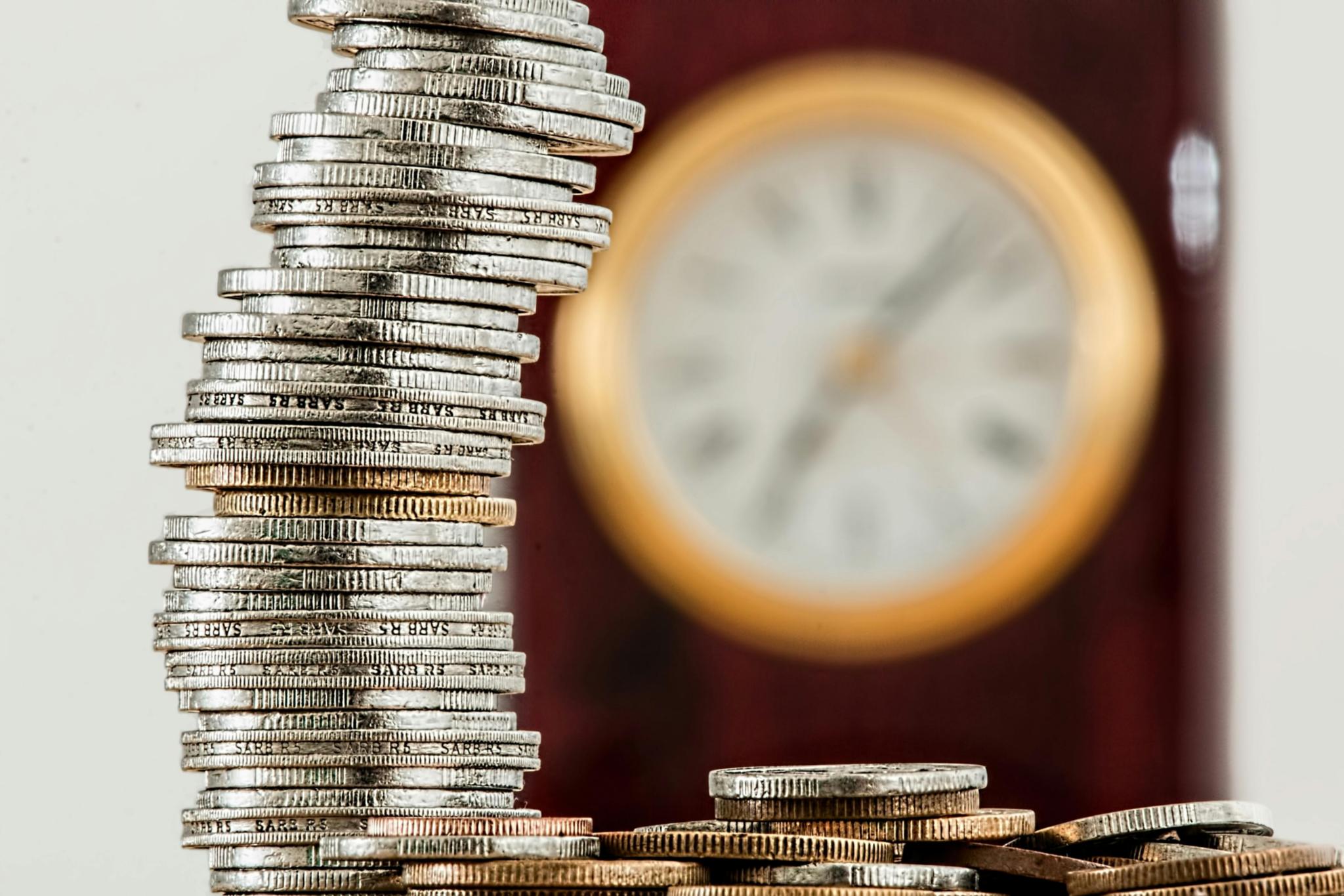 Münzstapel mit Uhr im Hintergrund